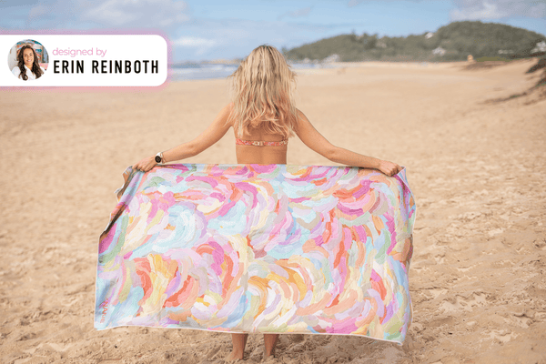 Recycled sand-free beach towel with multicolor abstract brushstroke pattern, held open on beach