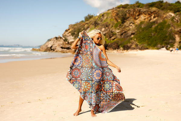 Recycled sand-free beach towel with multicolour geometric tile pattern, draped on woman at beach.