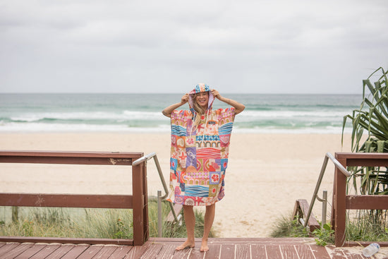 Woman wearing a Nakie Retro Shores hooded towel enjoying ocean views from a coastal lookout.