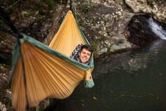 Person relaxing in a Nakie hammock suspended above a river