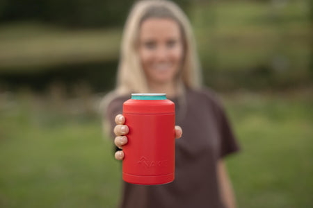 Red cylindrical cooler cup with turquoise lid, held in hand against outdoor background