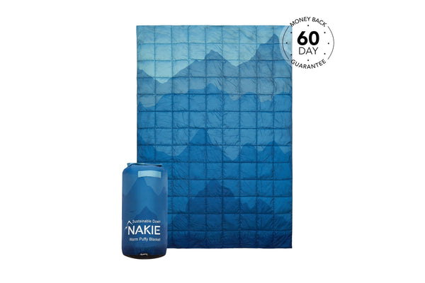 Blue quilted puffy blanket with mountain pattern, shown unfolded next to its compressed carrying case.