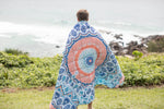 Sustainable down puffy blanket with blue and coral mandala pattern, worn as wrap over shoulders by ocean. preview #9