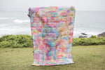 Colorful quilted puffer blanket with watercolor floral print in pink, blue, yellow, and green tones, displayed outdoors. preview #3