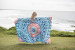 Blue and coral mandala-print sustainable down puffy blanket held up outdoors overlooking ocean. preview #2