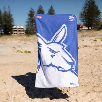 North Melbourne Kangaroos blue beach towel with white kangaroo logo and AFL branding, displayed on sand.