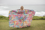 Multicolored quilted puffy blanket with abstract watercolor print, displayed open on grass overlooking ocean. preview #6