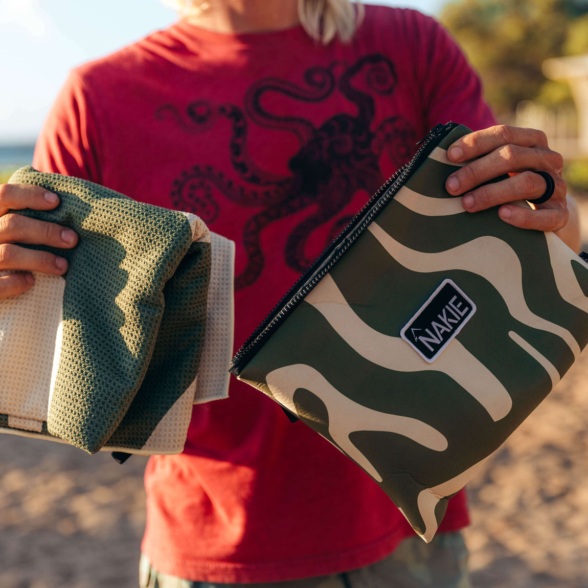 Eucalyptus green recycled beach towel with cream wavy pattern, held up at beach by person wearing red shirt