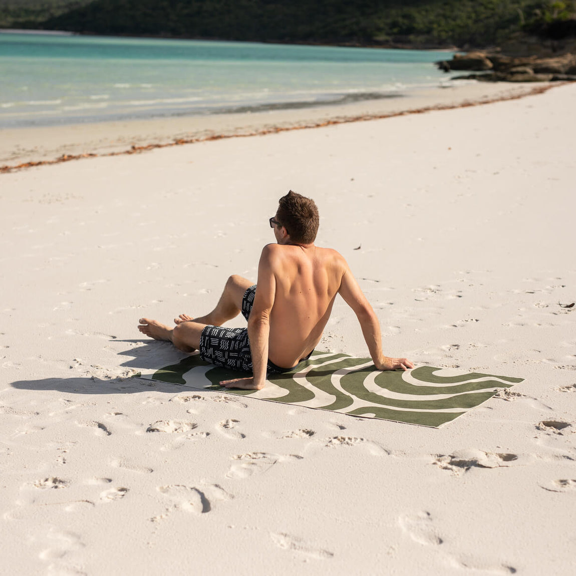 Eucalyptus green wave-patterned beach towel with recycled material, displayed on sand at tropical beach