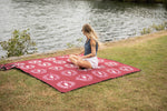 Burgundy picnic blanket with white circular Ringers Western logos spread on grass by water preview #7