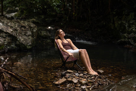 Woman leaning back in the Rosy Tides Camping Chair in a creek