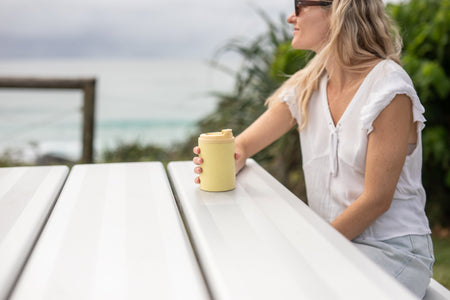 Daisy Yellow Cooler & Coffee Cup held on a picnic table by the beach