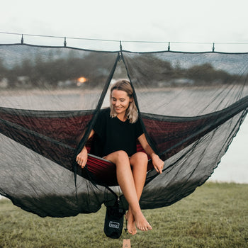 A woman relaxing in a Nakie hammock covered by our Bug Net, enjoying a peaceful outdoor experience protected from insects.