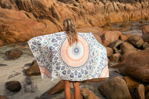 Recycled sand-free beach towel with blue and orange geometric mandala pattern, worn by person at rocky beach