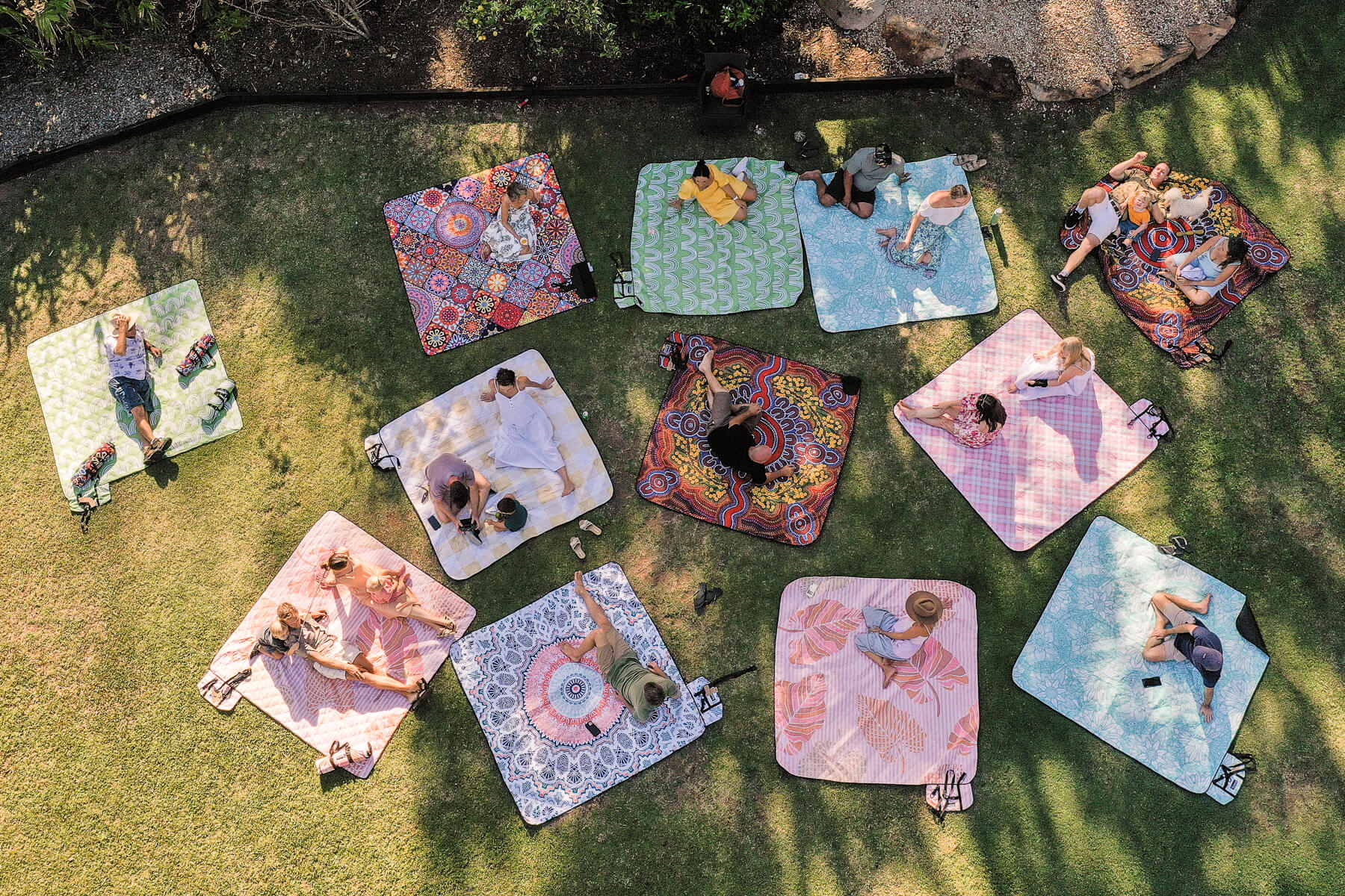 Image of people sitting or lying on Nakie's recycled picnic blankets in different colors, enjoying outdoor gatherings with comfort and sustainability.